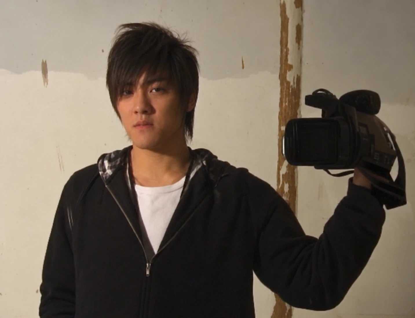Young Stanley Yang with long hair holding a video camera in Shanghai